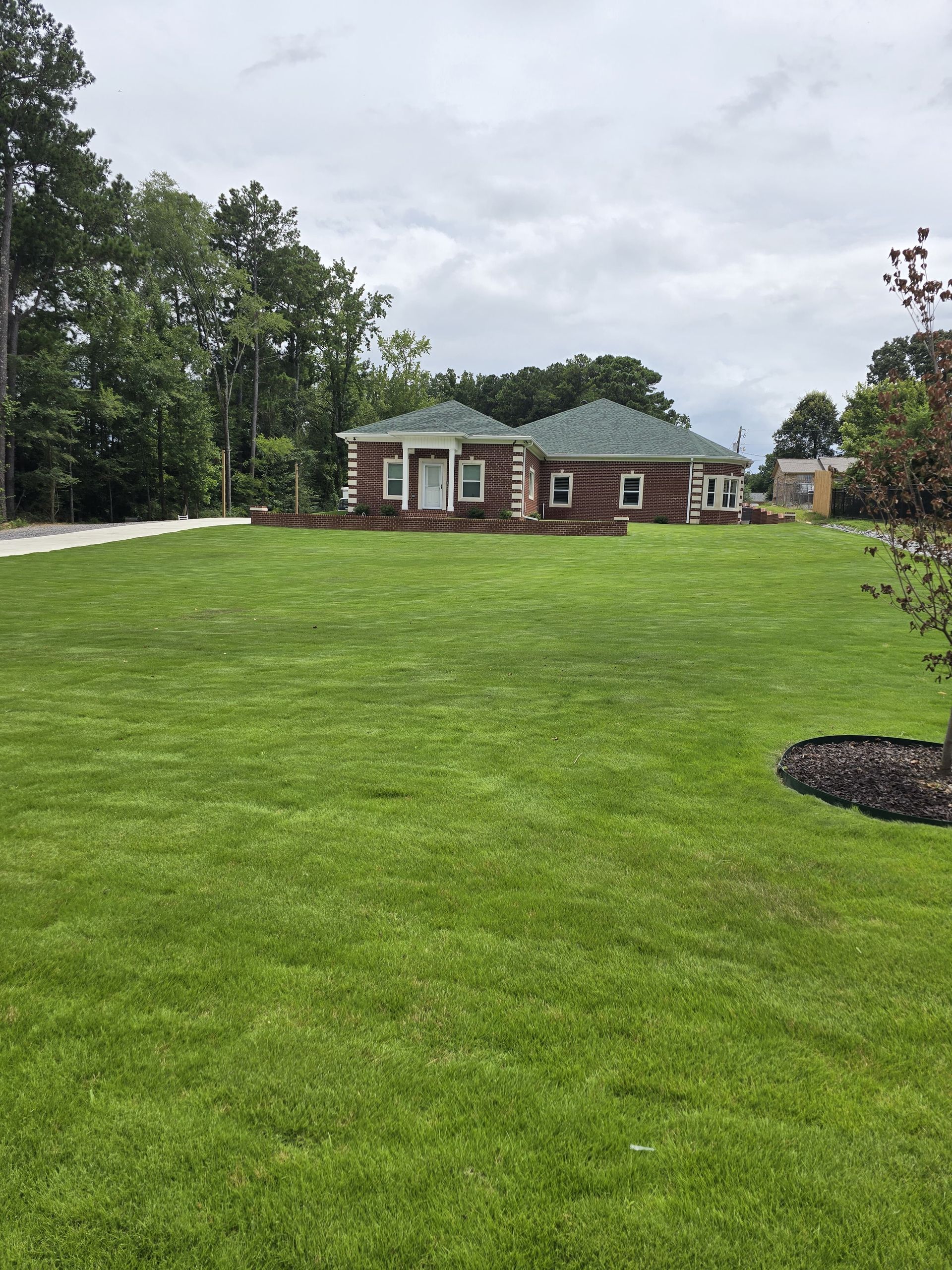 Log cabin style house with green lawn and trees under a cloudy sky.