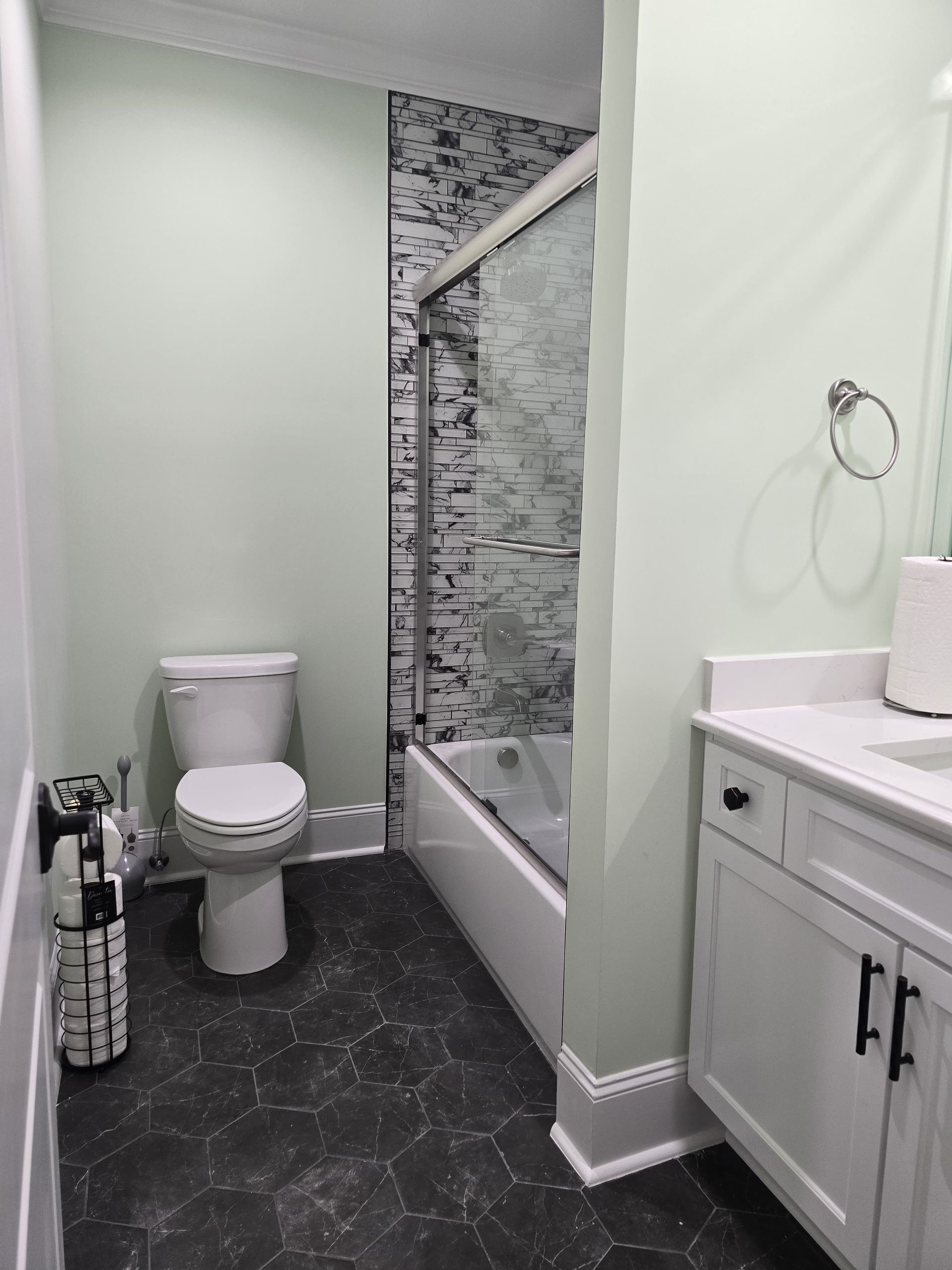 Small bathroom with pale green walls, dark floor, toilet, and vanity with a tub/shower.