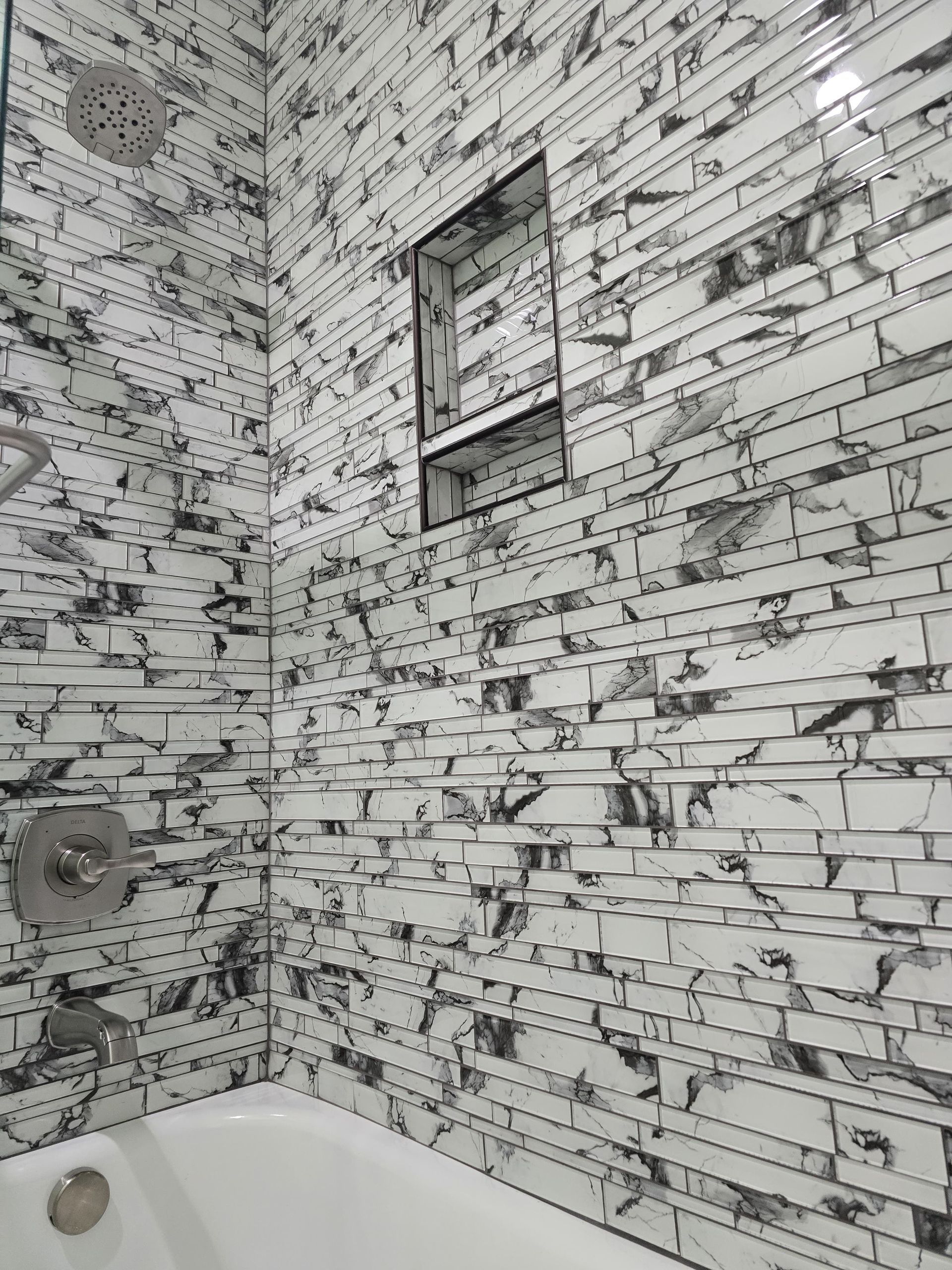 Shower with white and black patterned tile, recessed shelf, and silver fixtures.