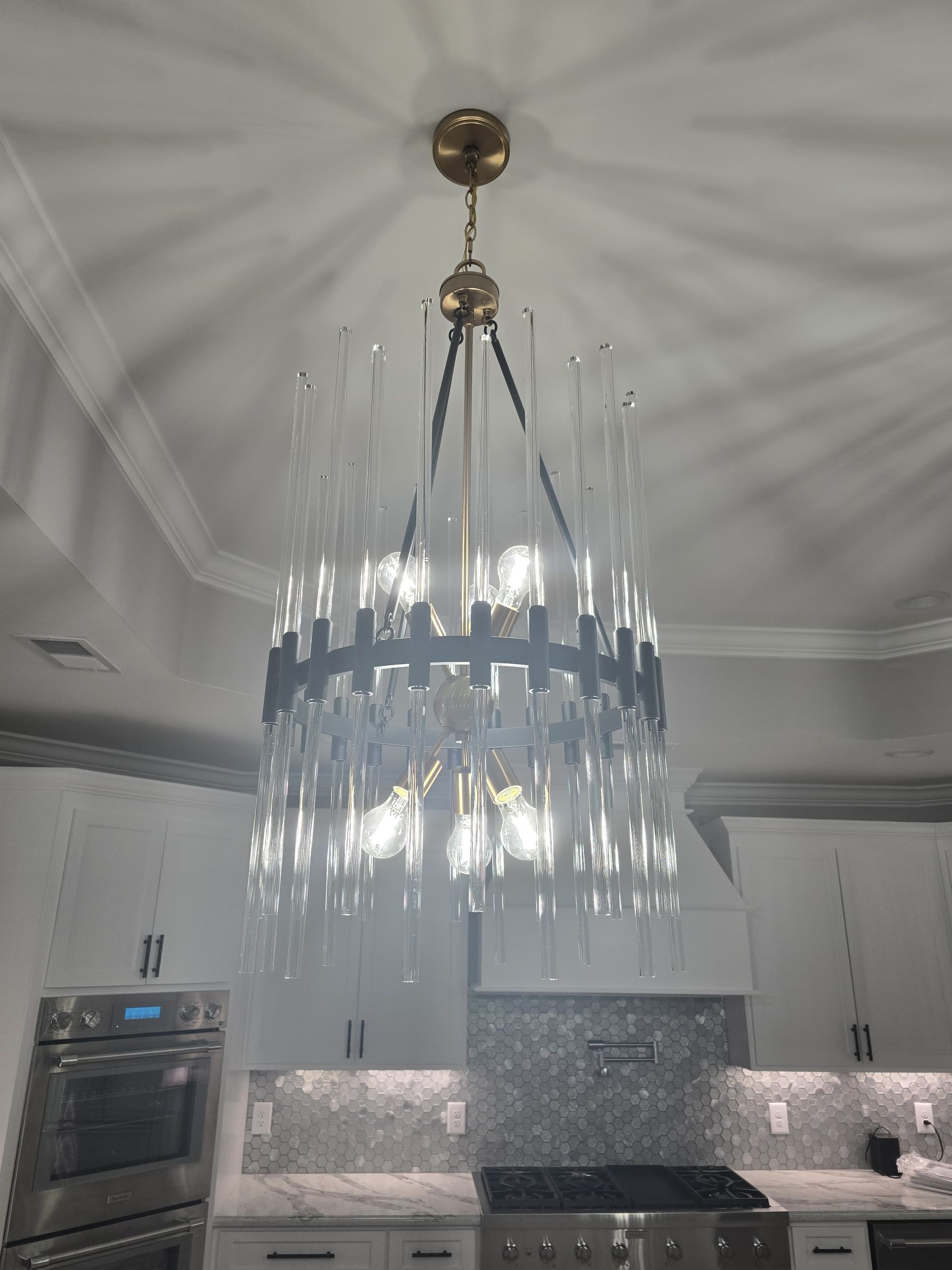Modern chandelier in a kitchen with white cabinets and a tiled backsplash.