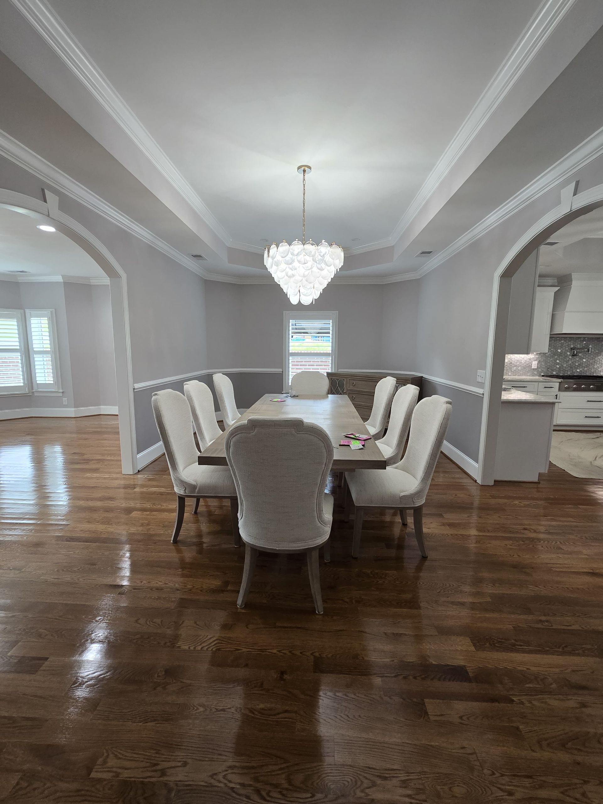 Dining room with a table and chairs, wood floors, gray walls, and a chandelier.