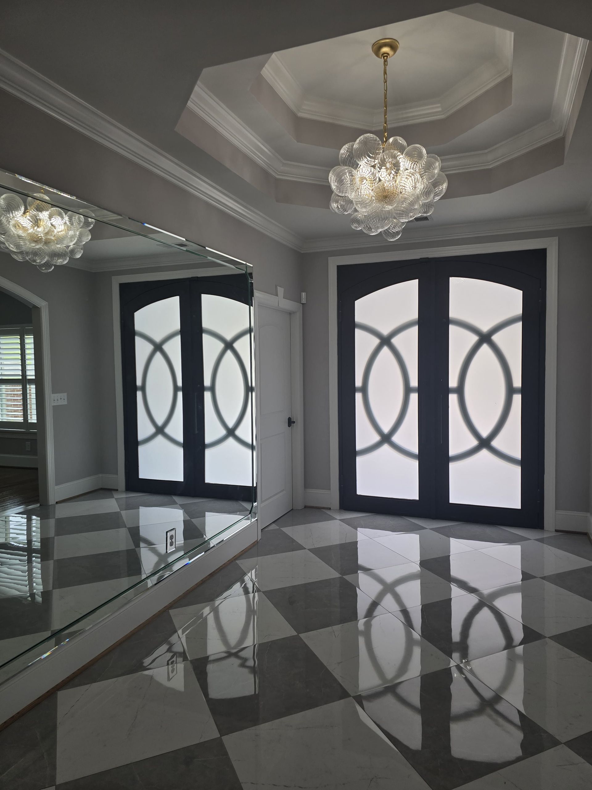 Elegant room with mirrored wall, black doors, and checkered floor, reflecting light from chandelier.