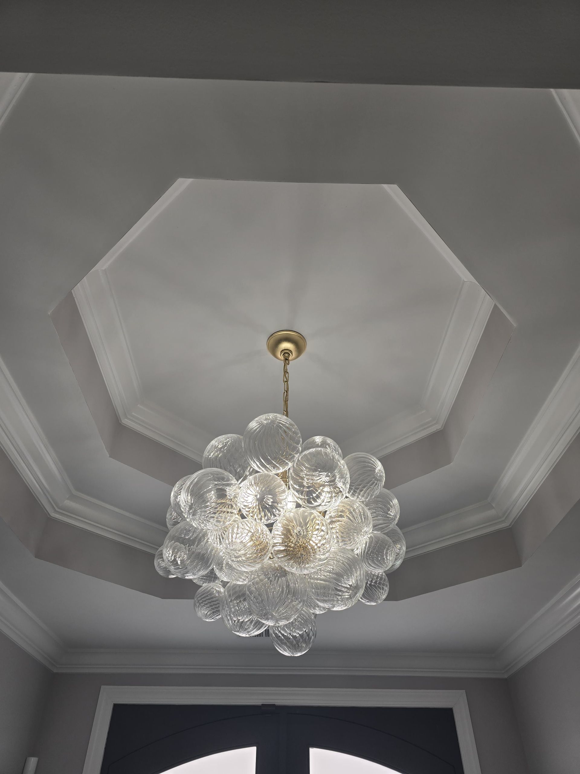 Chandelier hanging from a multi-layered octagonal ceiling. Ornate glass globes, white ceiling, gold fixture.