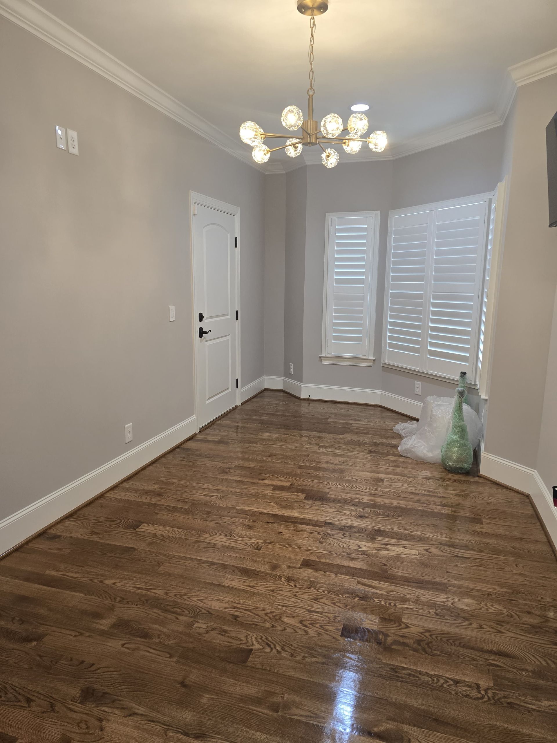 Empty room with hardwood floors, gray walls, white trim, and a chandelier.