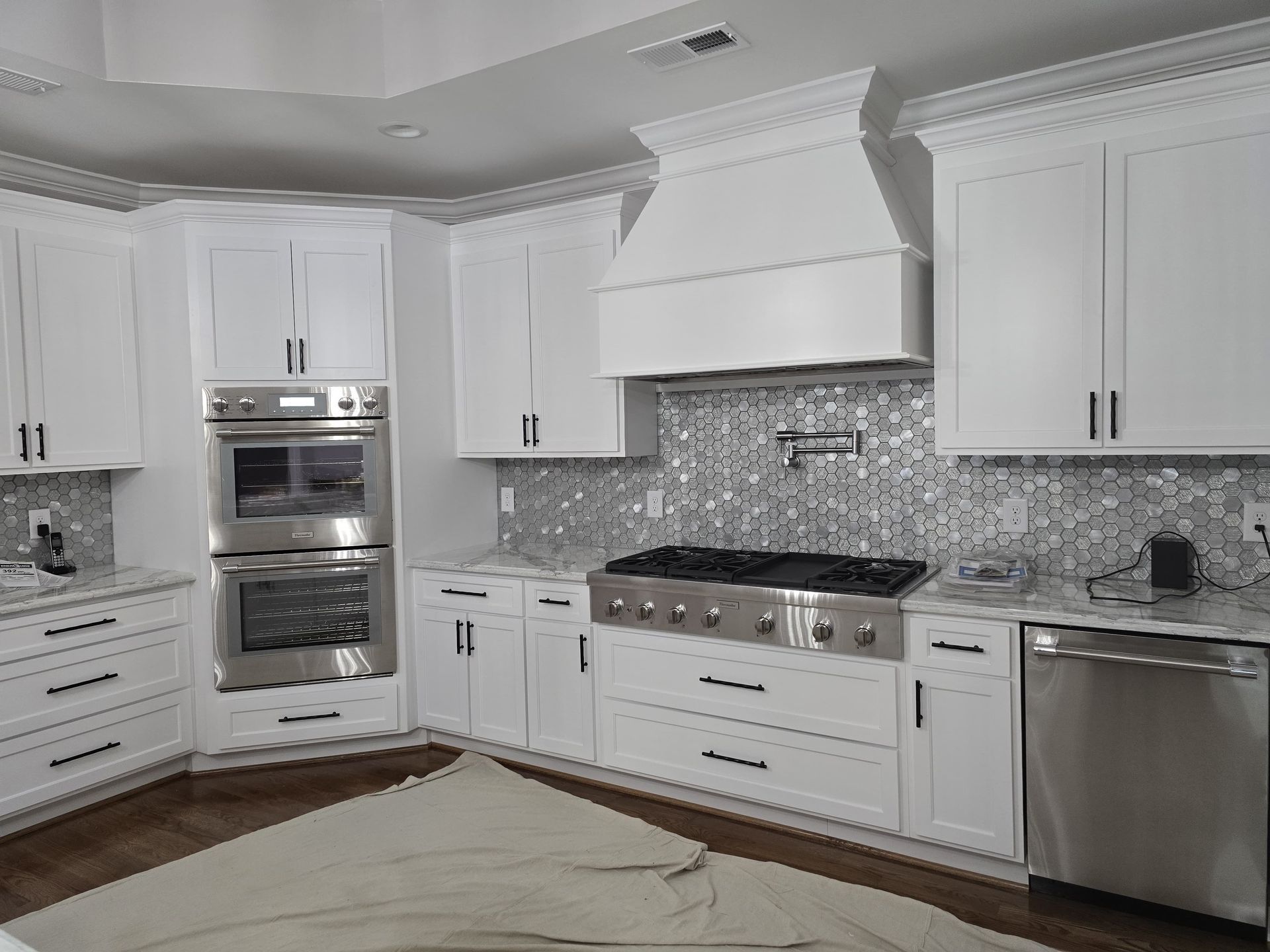 White kitchen with stainless steel appliances, cabinetry, and range hood.