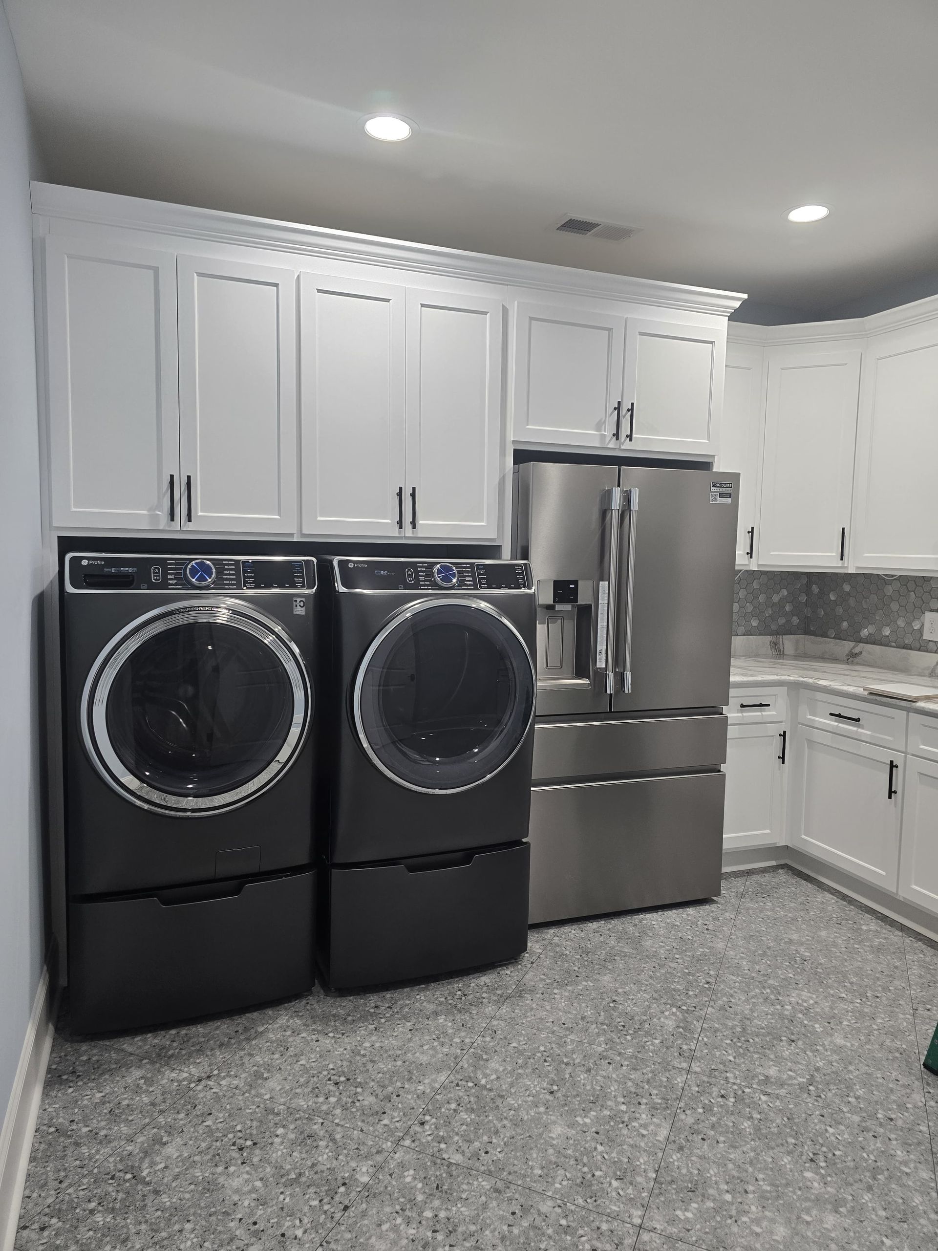 Laundry room with white cabinets, gray appliances, and speckled floor.