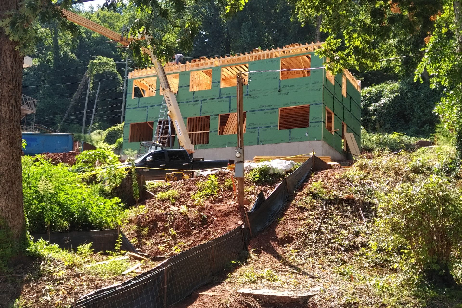 Construction of a two-story building on a hillside. Green siding and wooden framing visible. Crane nearby.