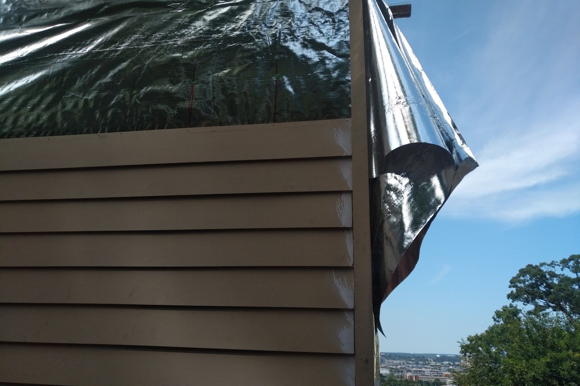 Exterior of building with silver reflective material and beige siding against a blue sky.