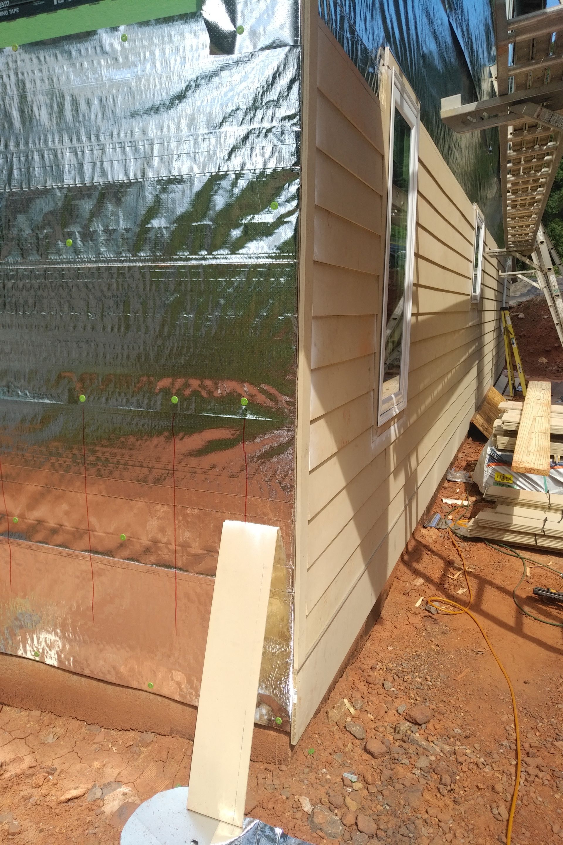Construction site: Building's siding being installed. Brown siding next to shiny metallic sheathing.