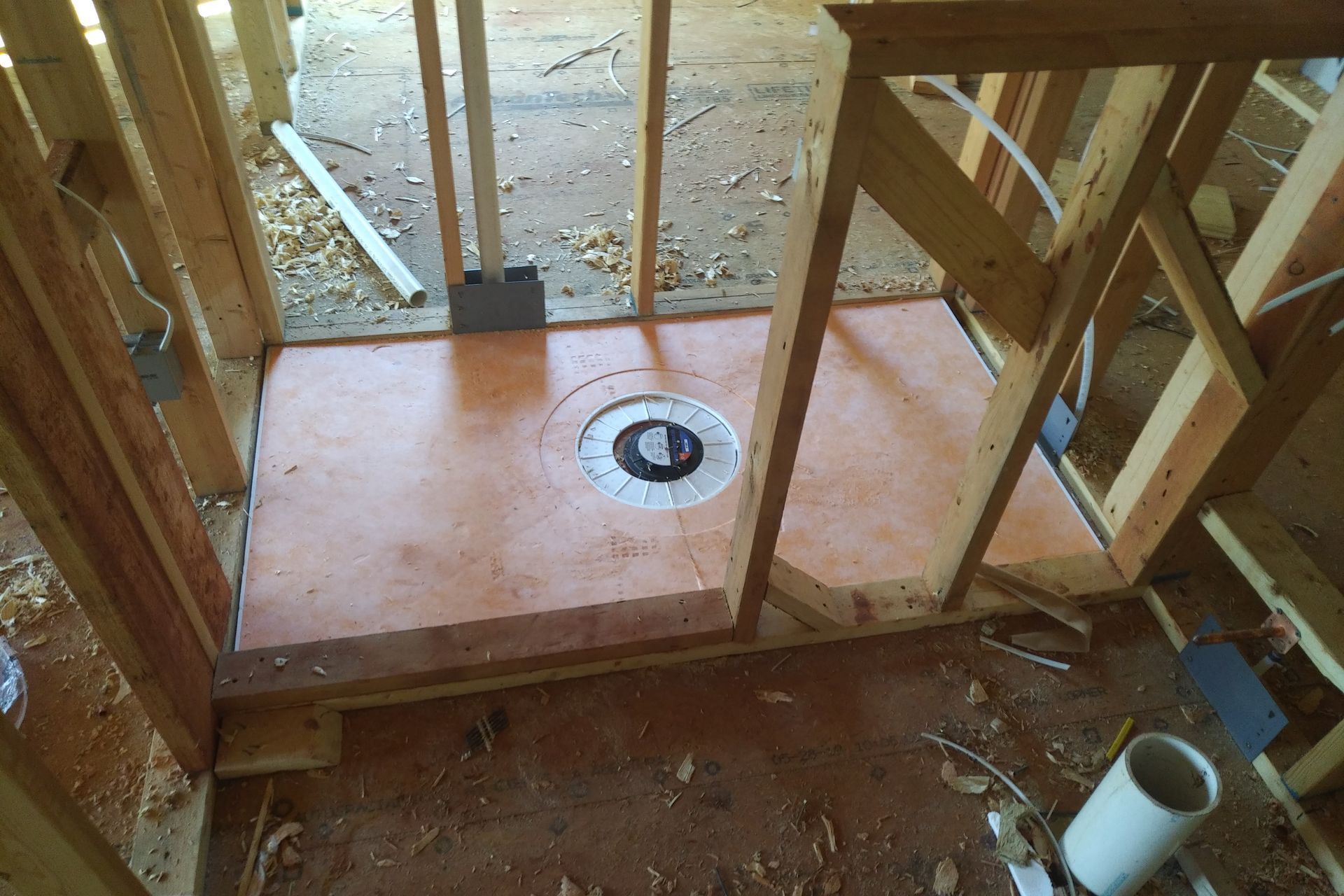 Framed shower stall under construction; brown base with drain, wooden beams, plumbing.