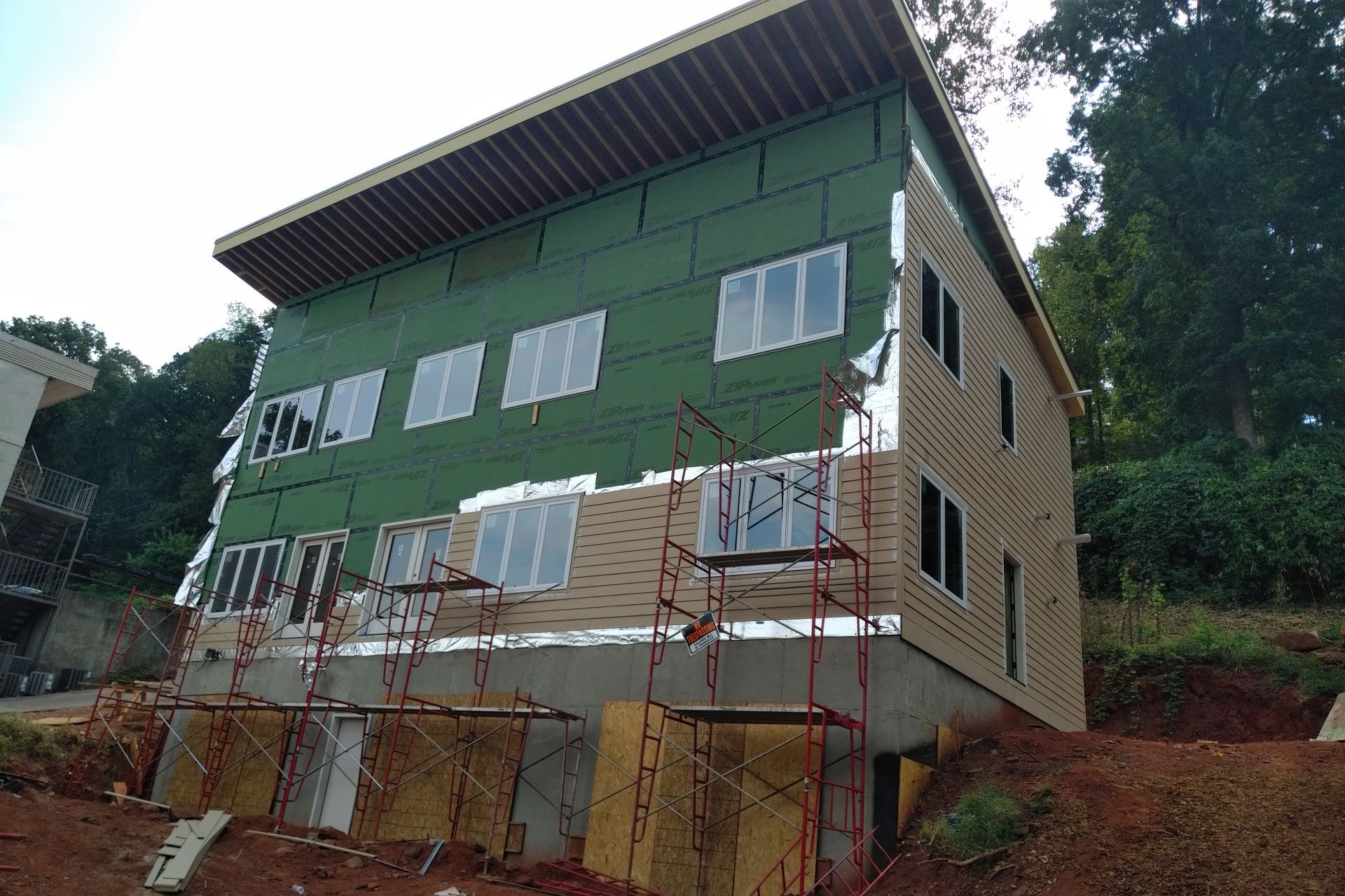A three-story building under construction with green and tan siding, windows, and scaffolding.