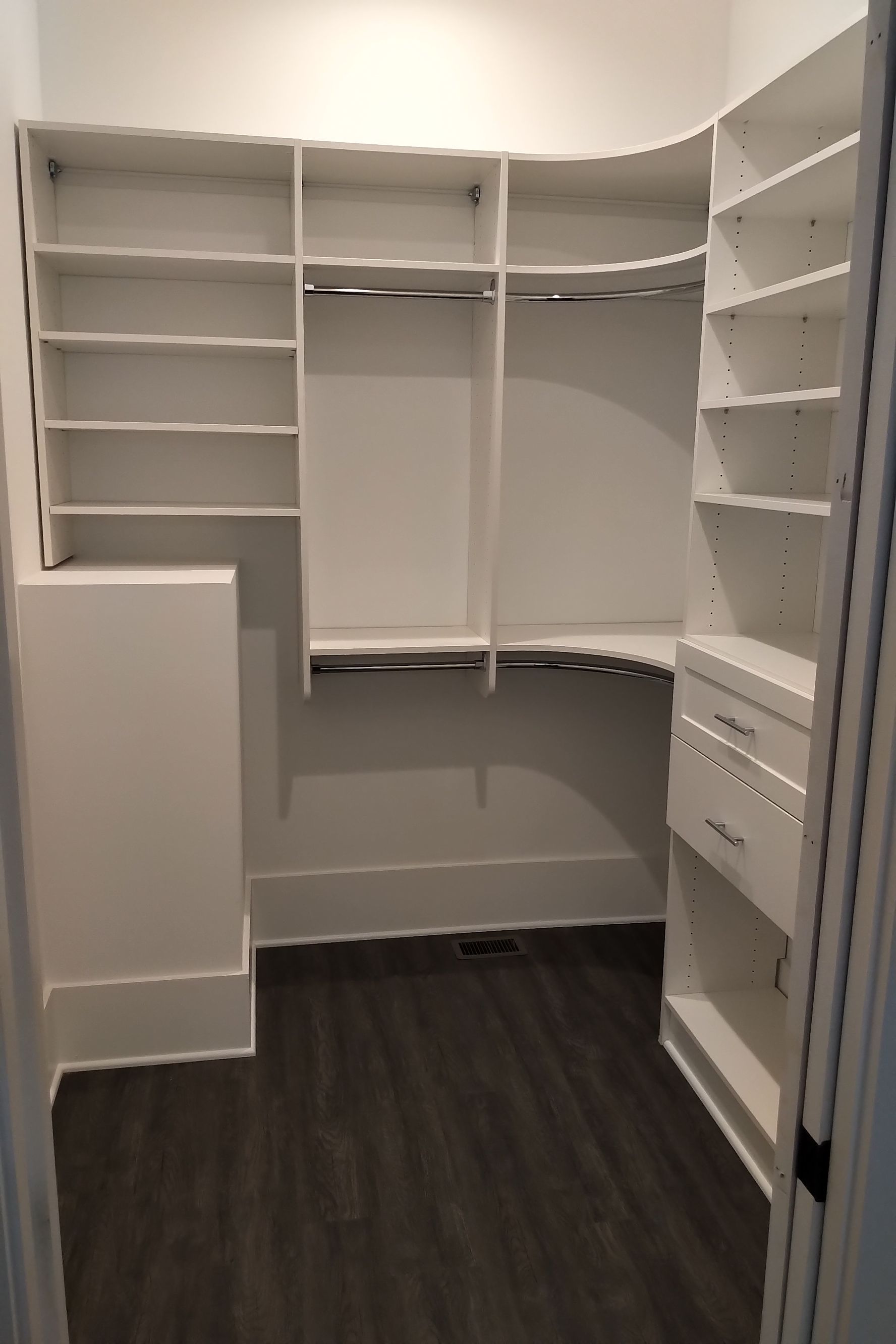 White built-in closet with shelves, rods, and drawers in a room with dark flooring.