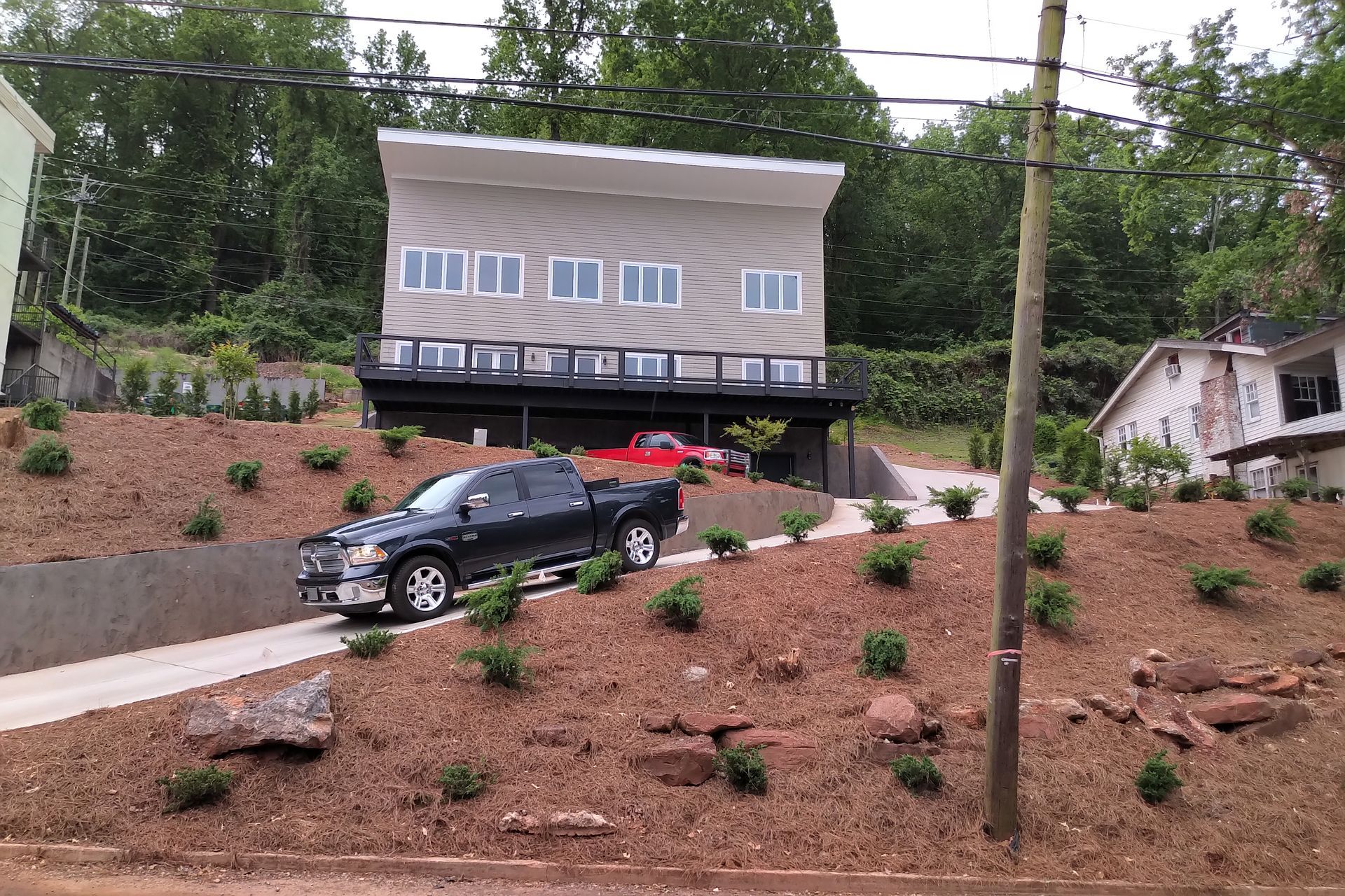Dark pickup truck driving up a sloped driveway to a modern two-story house on a hill.