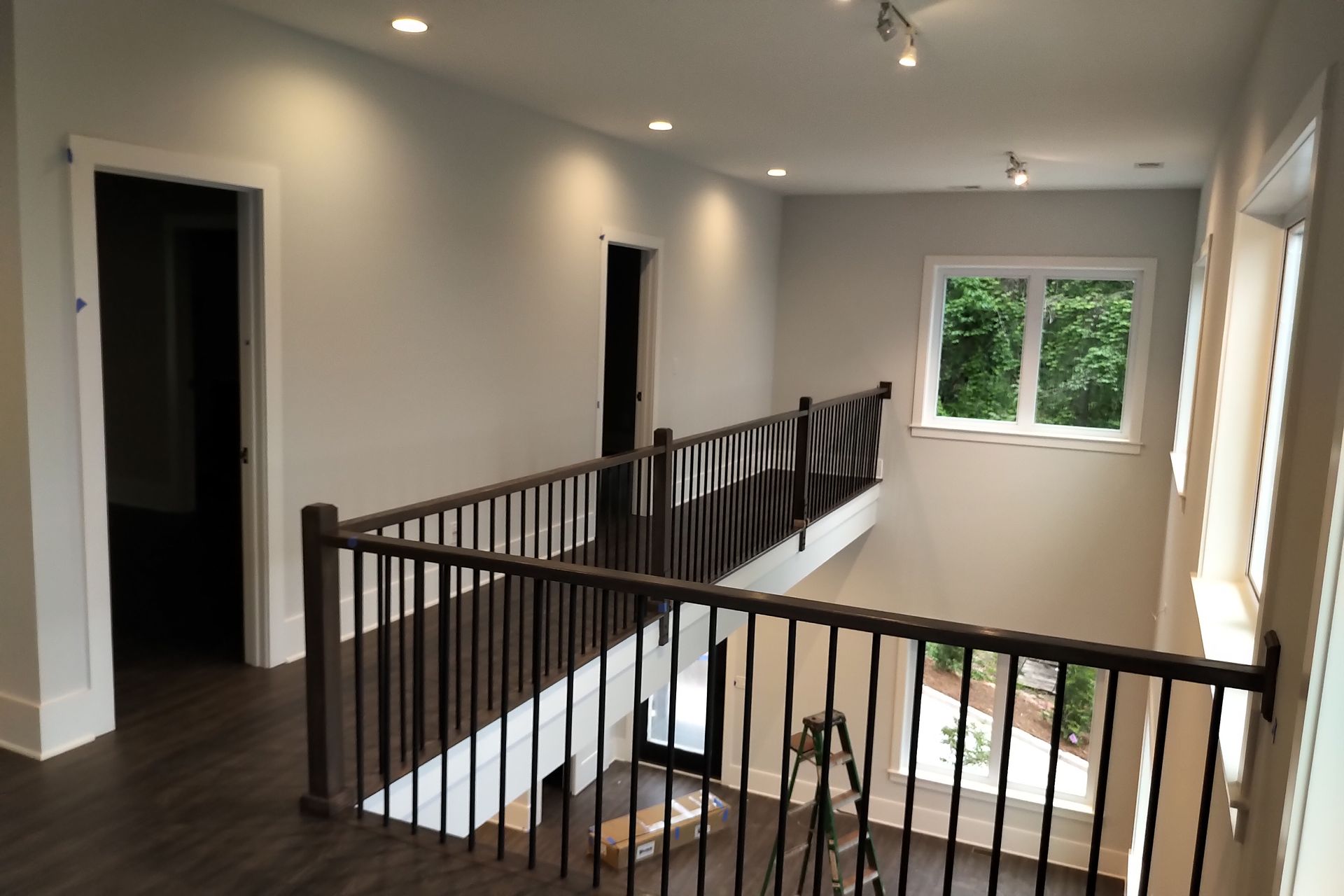 Interior hallway with a dark wood railing overlooking a lower level, with windows and recessed lighting.