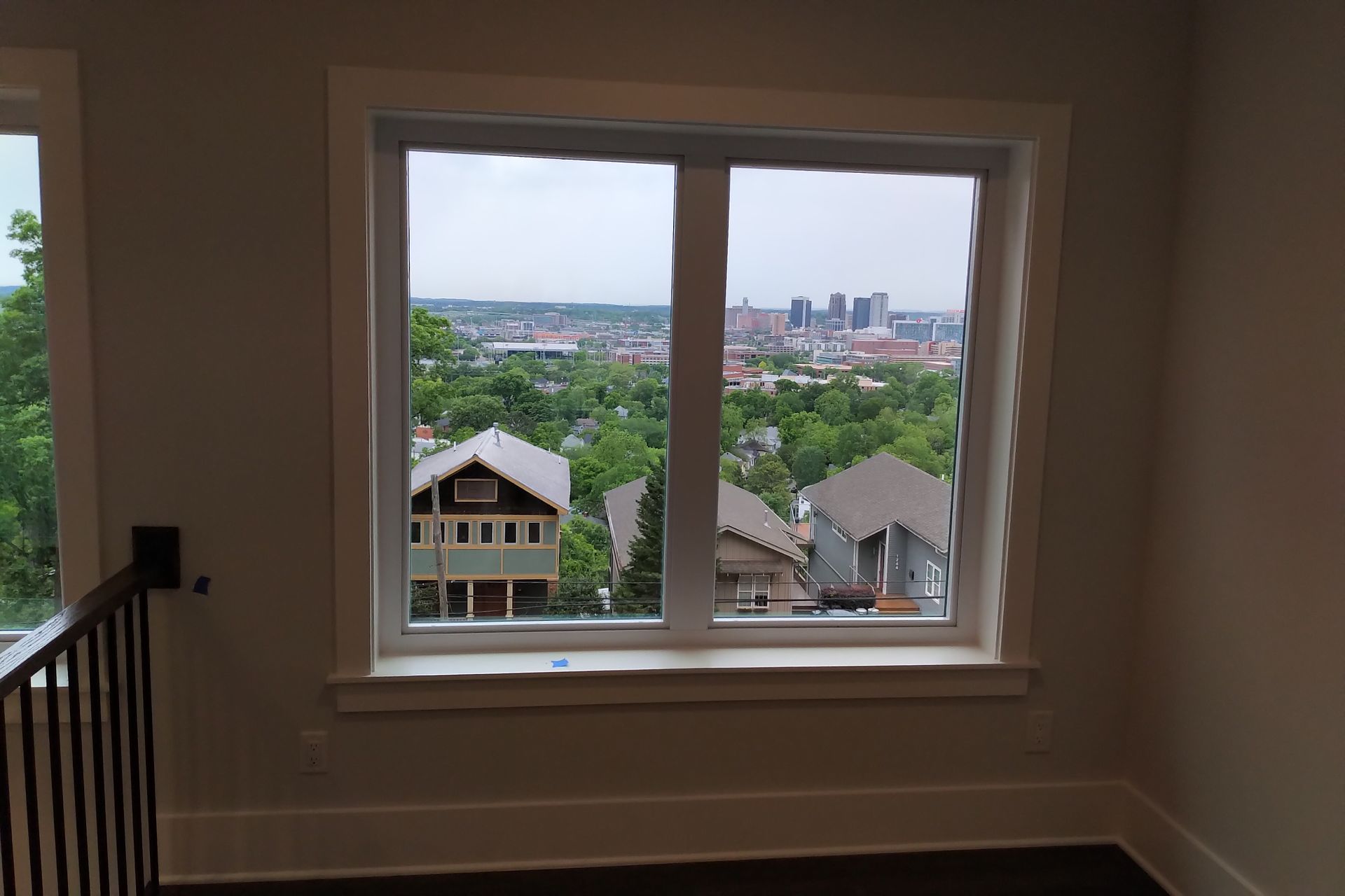 Window overlooking city and houses with green trees; a tan wall surrounds it.