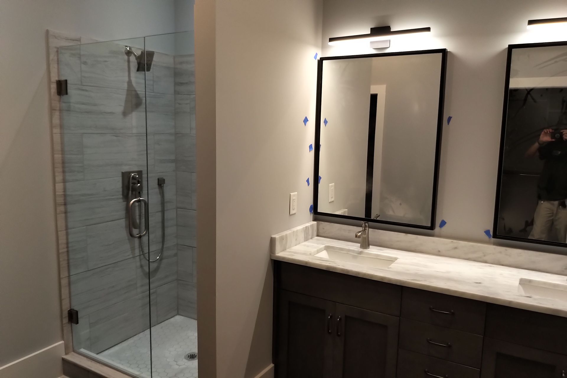 Bathroom with a glass shower, dark vanity, marble countertop, and mirrors.