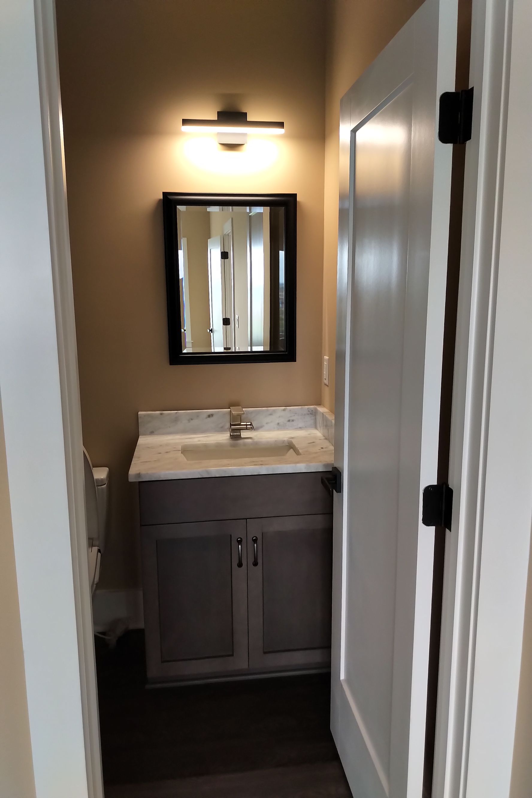 Small bathroom with gray vanity, mirror, and white door.