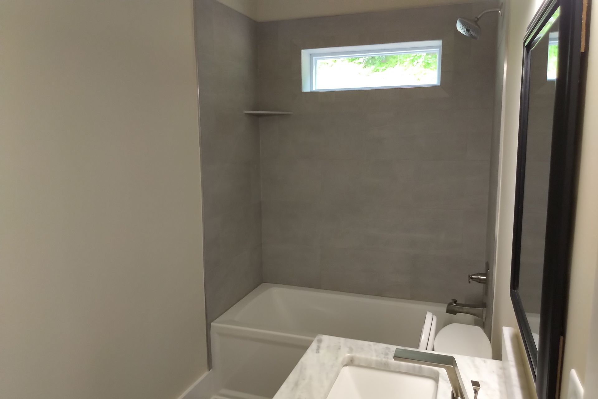 Bathroom with gray tile shower, white tub, sink, and toilet. Small window over the shower.