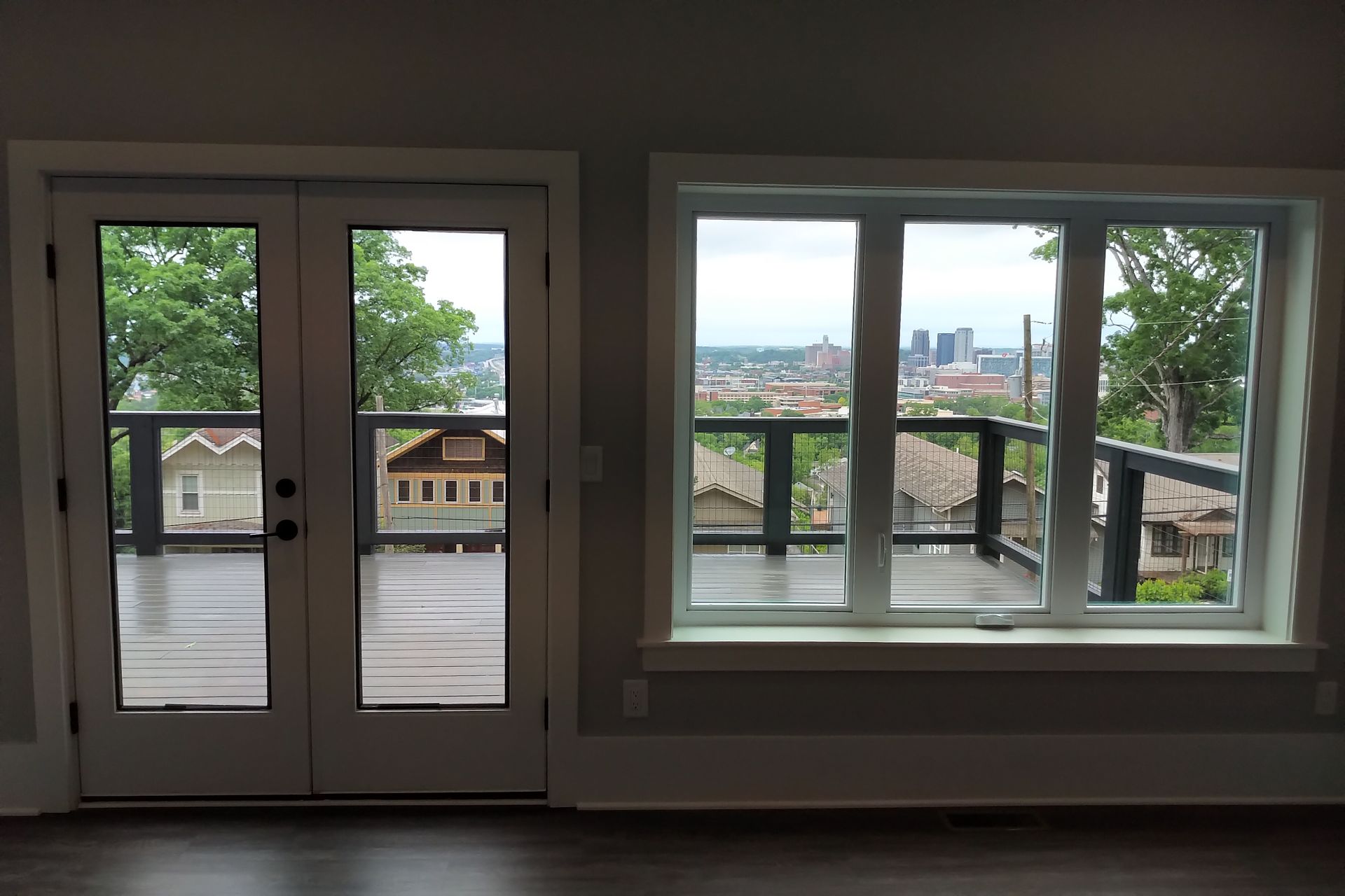 French doors and a window open onto a deck with city views, the sky is overcast.