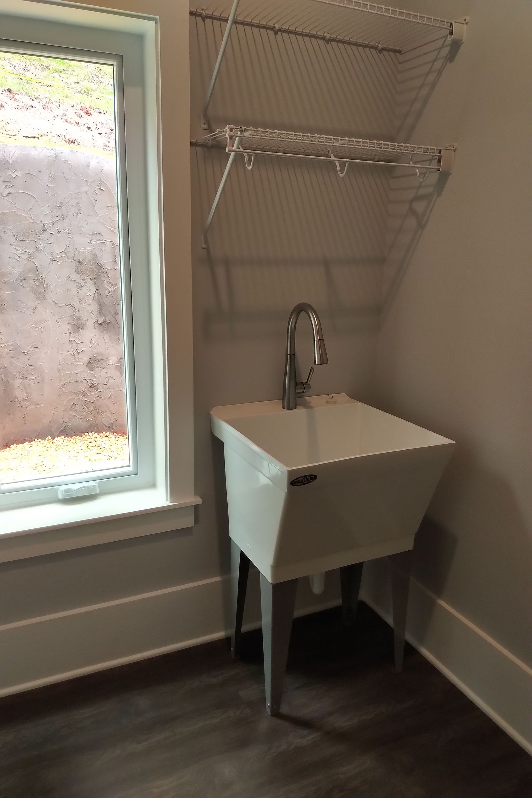 Utility sink in a laundry room with a window and wire shelving.