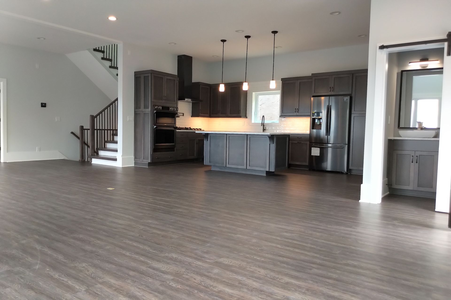 Spacious gray kitchen with island, dark cabinets, stainless steel appliances, and a staircase.