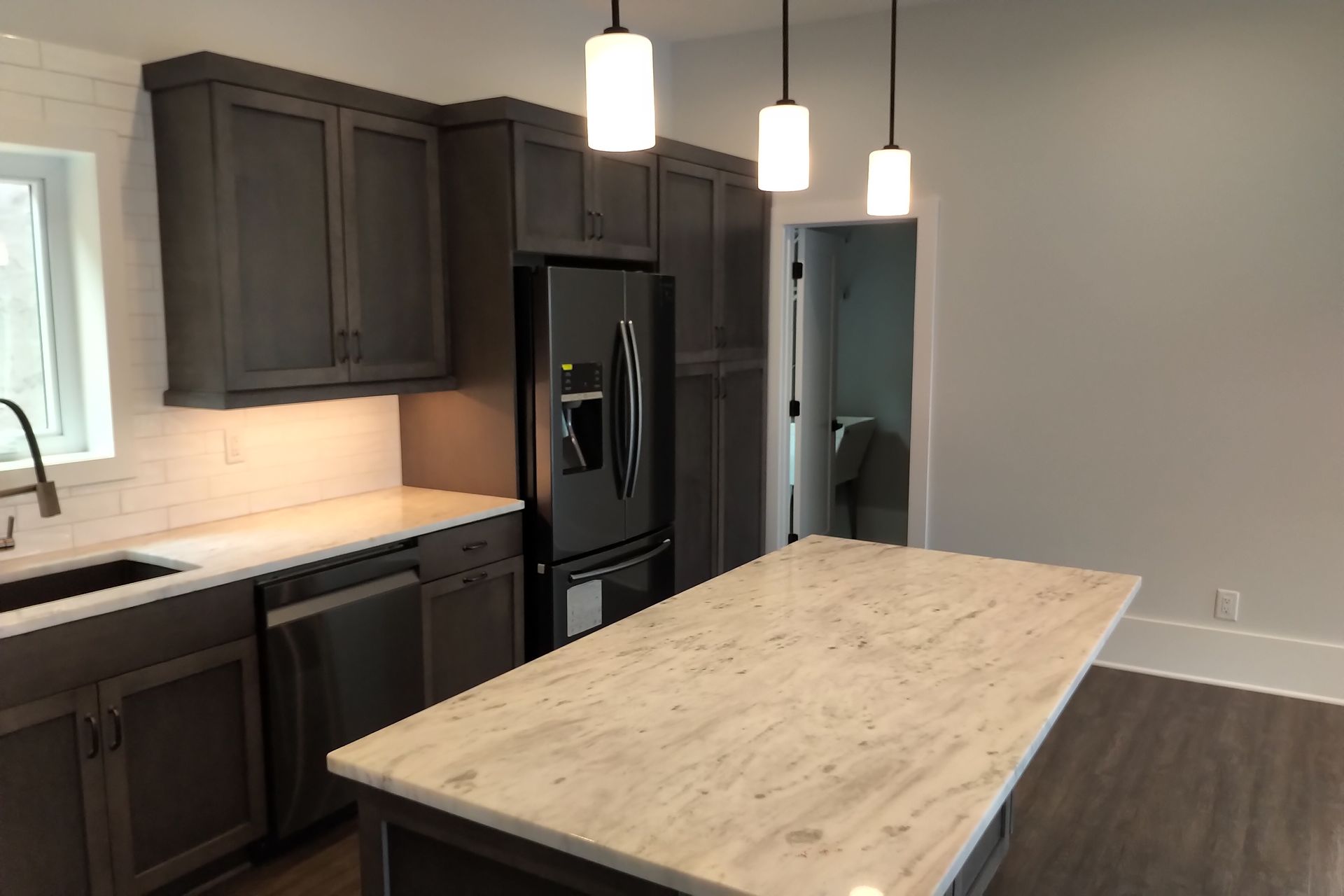 Dark gray kitchen with stainless steel appliances, white countertops, and a large island.
