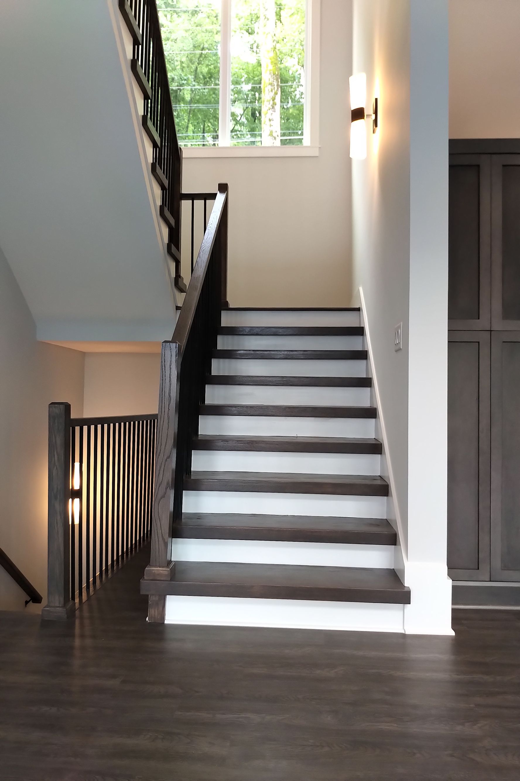 Staircase with dark wooden treads and railing. White walls and trim. Sunlight streams in from a window.