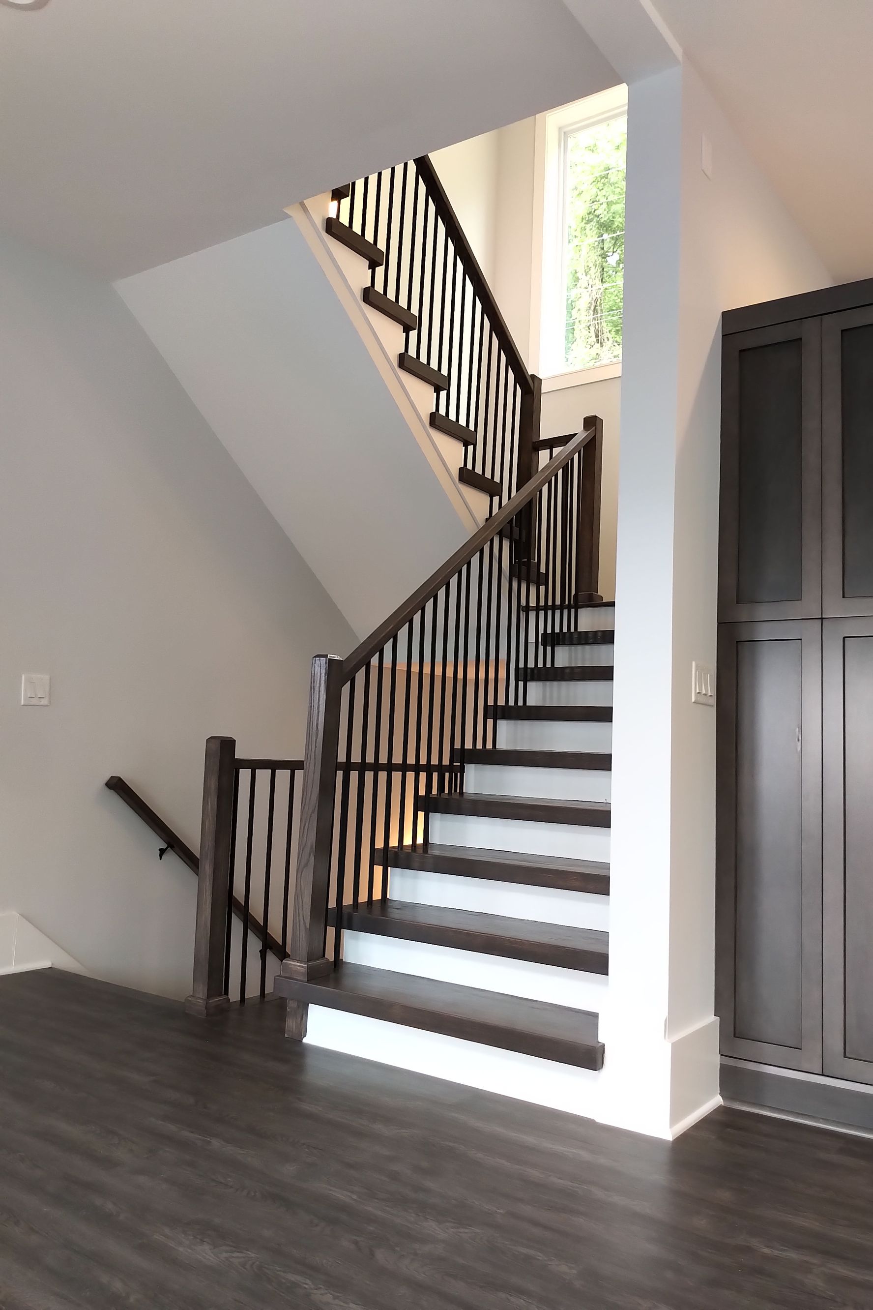 Staircase with dark wood steps and railing, white walls, and a window at the top.