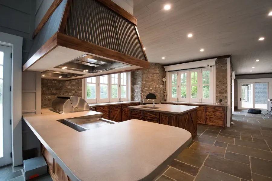 Rustic kitchen with gray countertops, stone walls, wood cabinets, and stainless steel range hood.