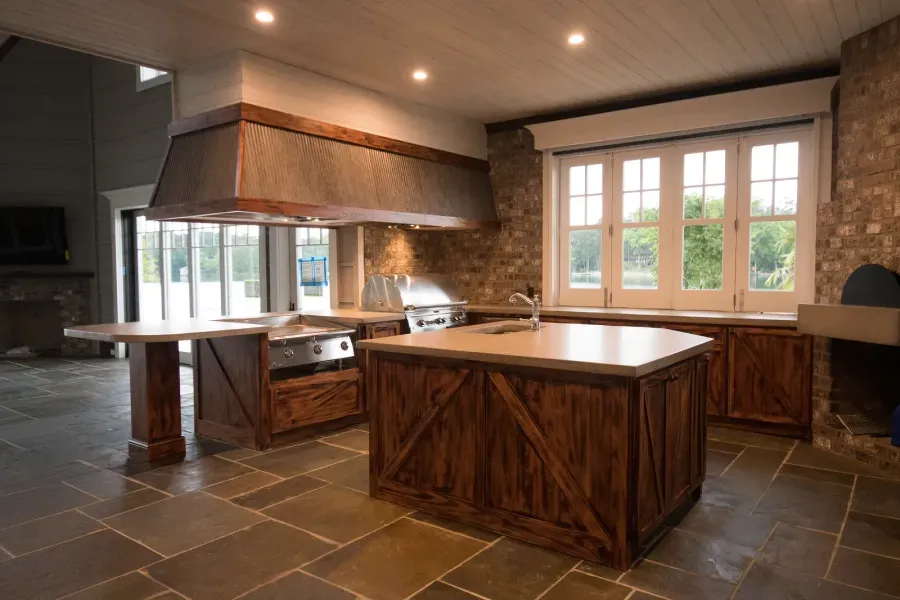 Rustic kitchen with wooden island and range hood, stone walls, and large windows.