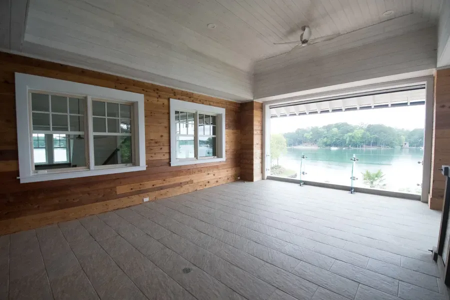 An empty porch with a lake view, wood walls, two windows, and open entry.