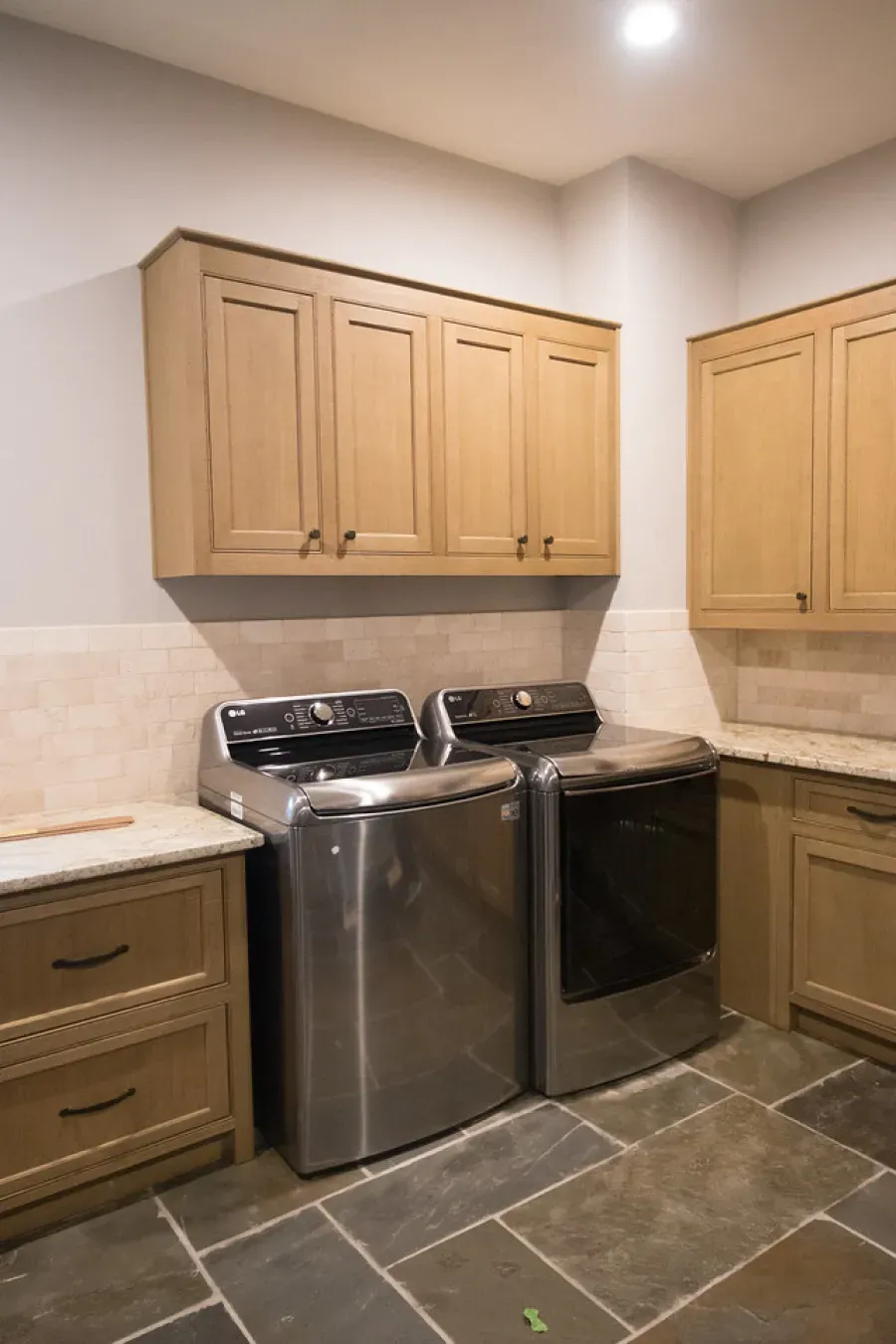 Laundry room with stainless steel washer/dryer, wood cabinets, stone floor.
