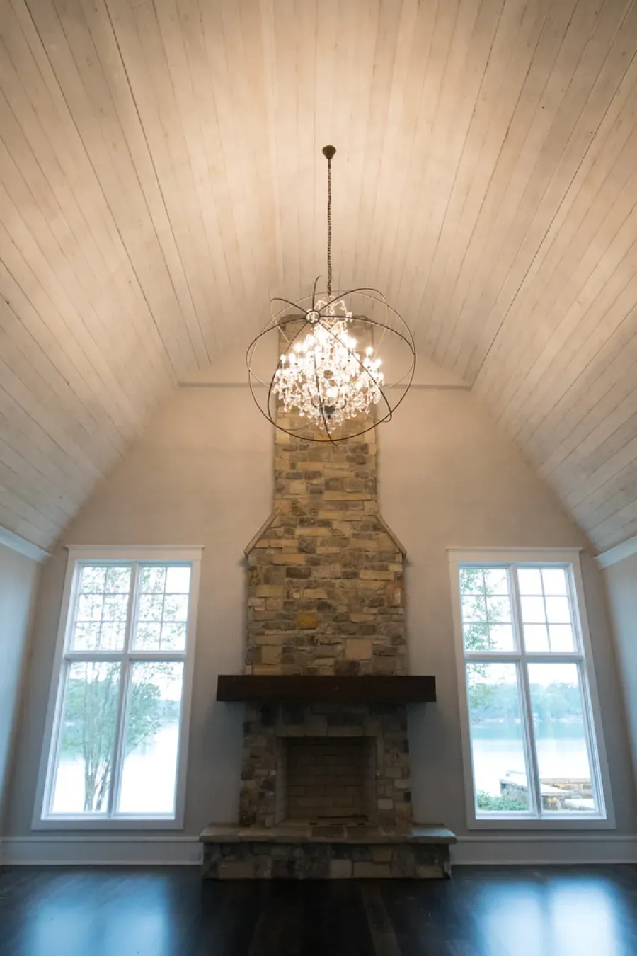 Living room with fireplace, windows, and ornate chandelier hanging from a wood-planked ceiling.