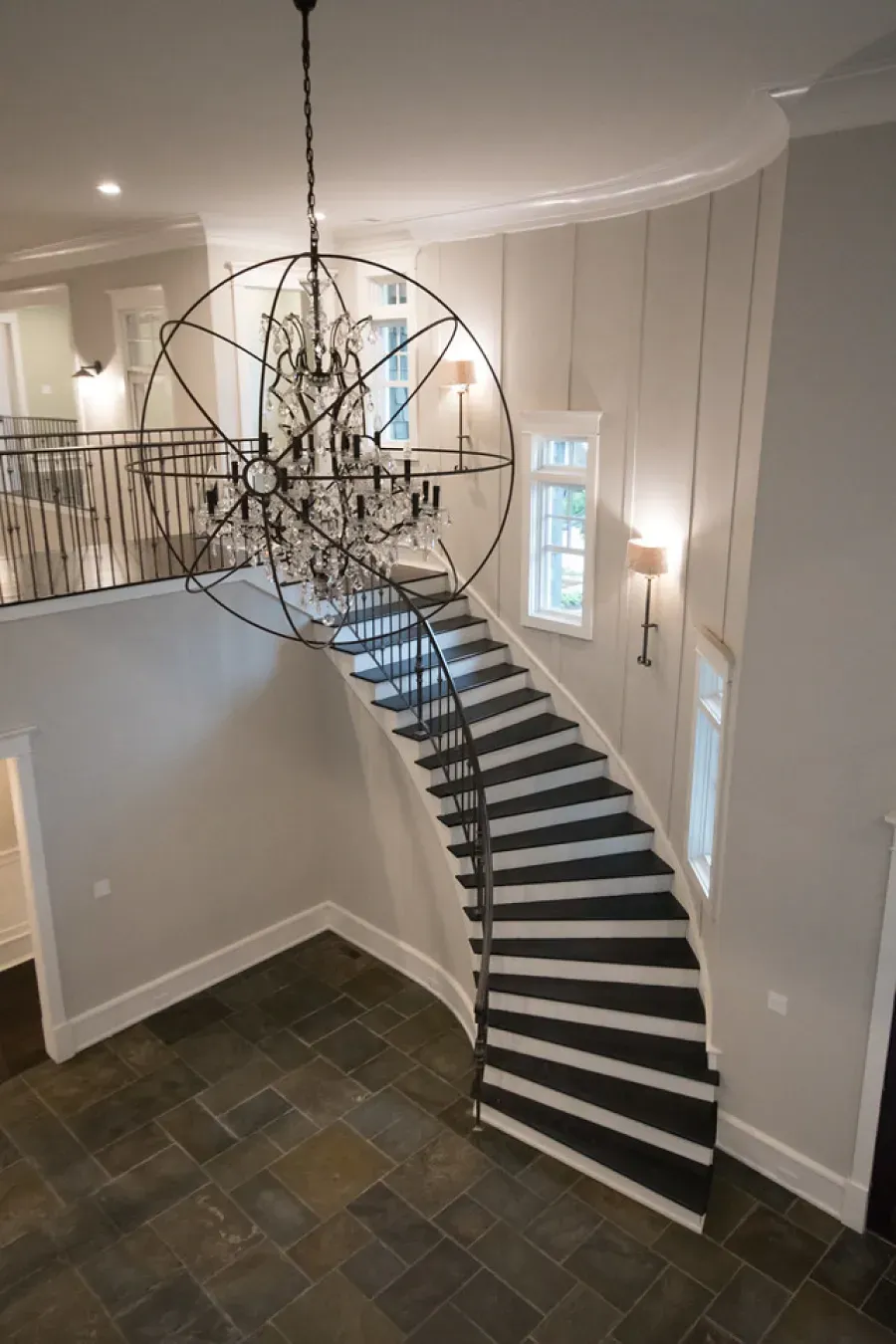 Grand foyer with curved staircase, large chandelier, and slate tile floor.