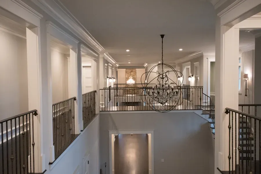 Hallway with iron railings, white columns, and a large chandelier.