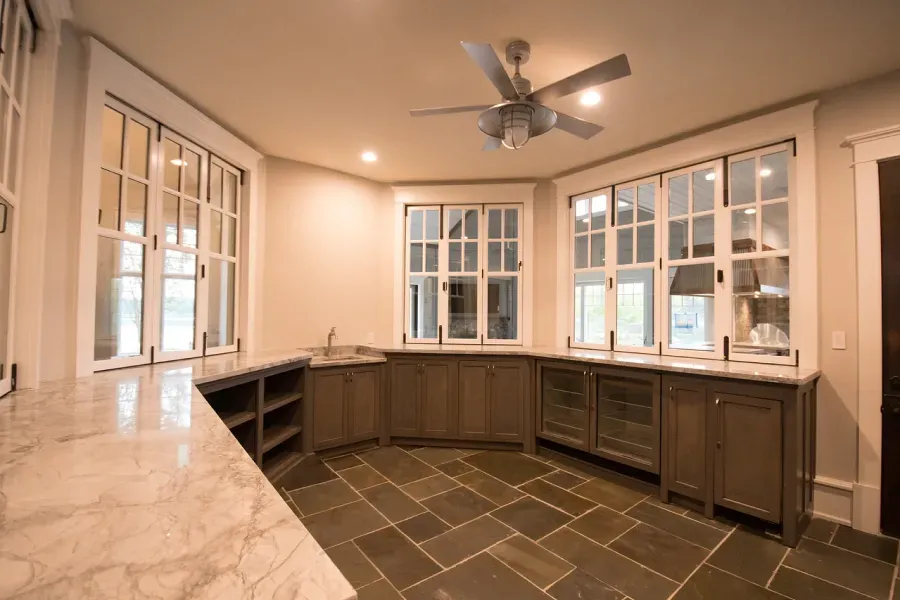 Bar area with marble counter, wooden cabinets, and large windows. Brown tile floor.