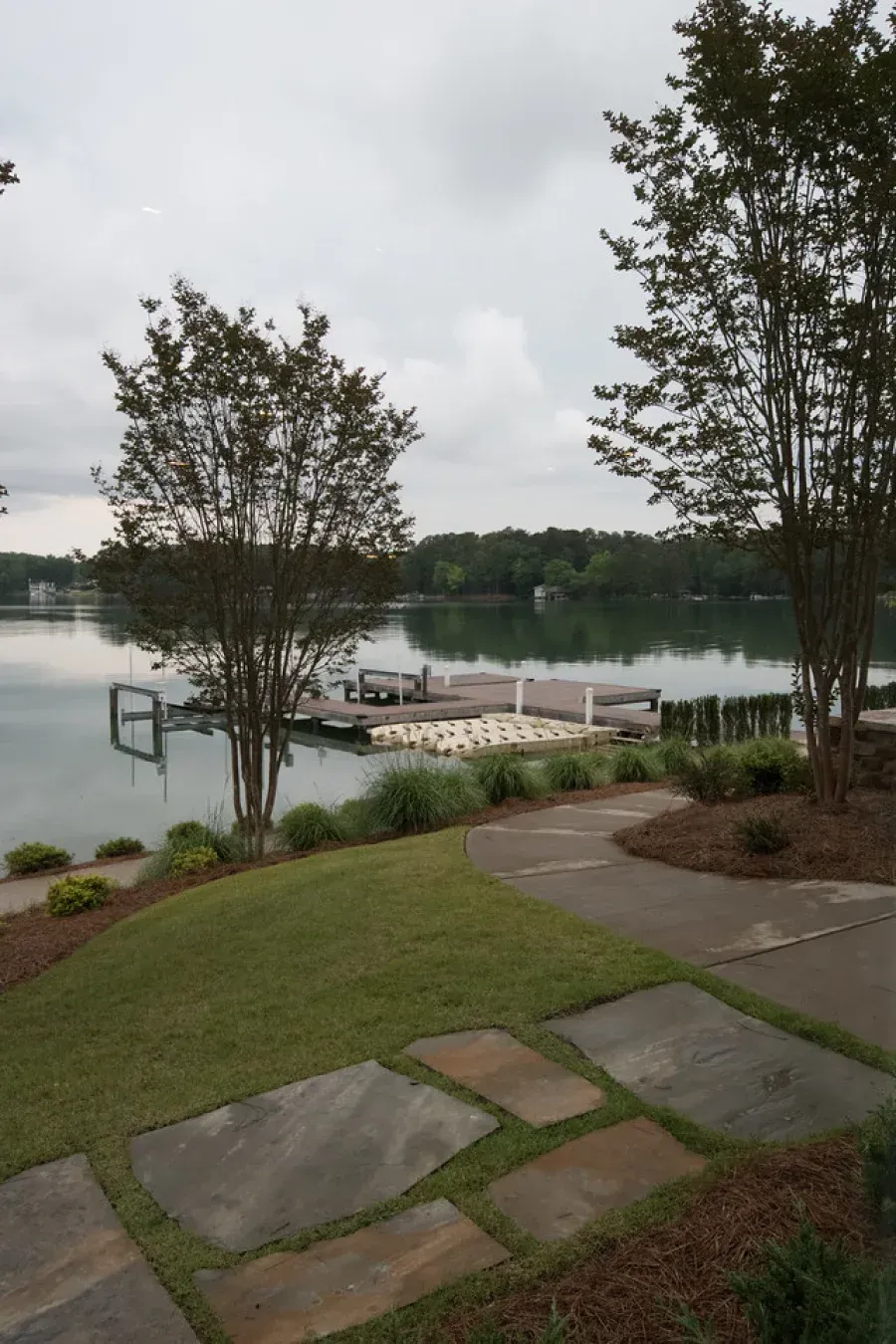 Lake scene with dock, trees, and walkway on a cloudy day.
