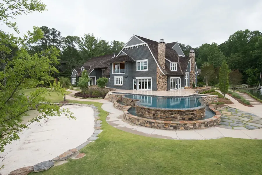 Large, gray-shingled house with a pool and sand trap in a green, wooded setting.