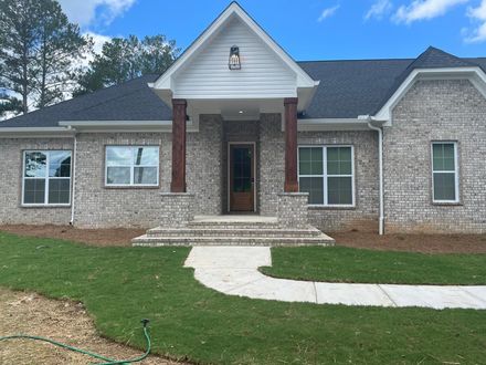 Brick house with white trim and dark roof; a concrete path leads to the front door.