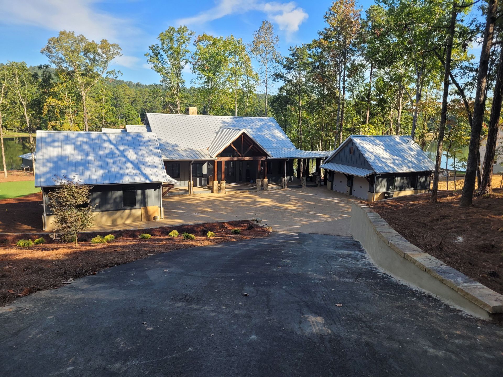 A rustic house with a white roof and a gravel driveway surrounded by trees and greenery.