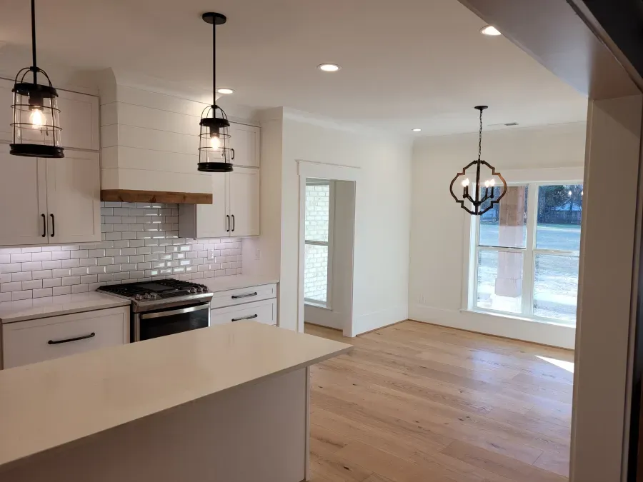 Modern kitchen with white cabinets, light wood floors, and pendant lights.