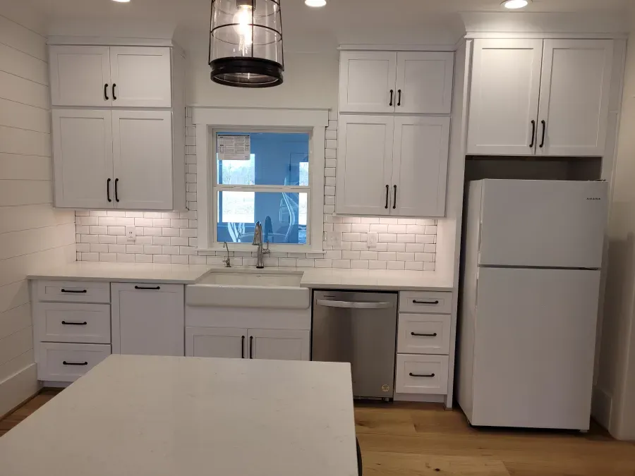 White kitchen with cabinets, sink, dishwasher, and a refrigerator; a window in the center.
