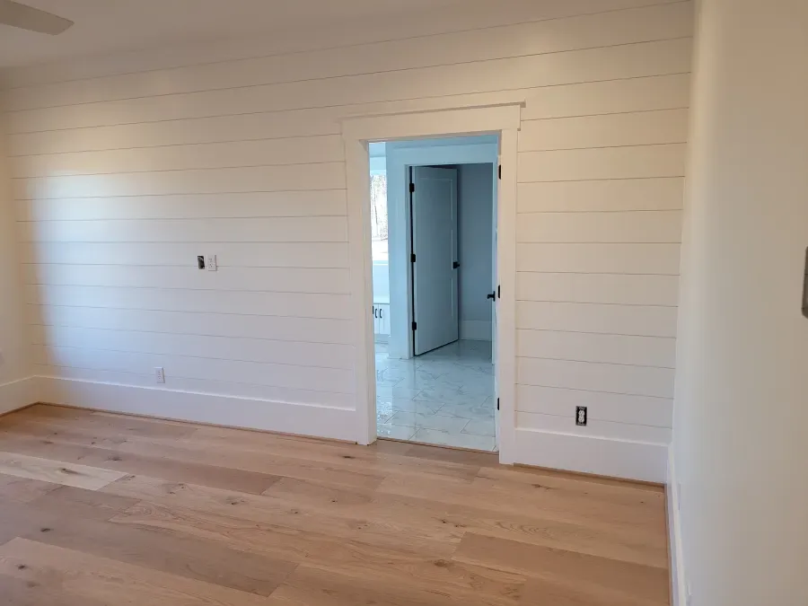 Room with light wood floor, white shiplap walls, and doorway to another room.