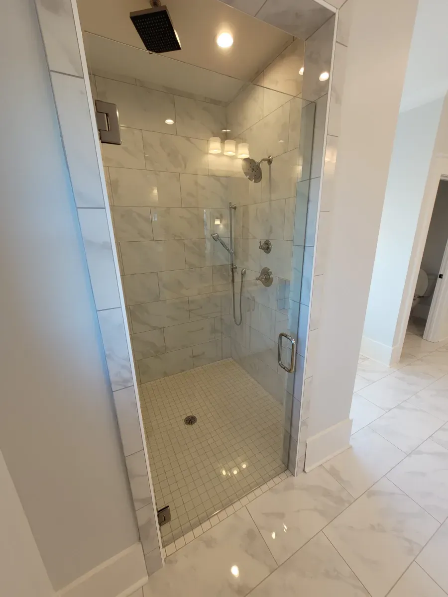 A modern bathroom with a glass shower door, white tiles, and chrome fixtures.