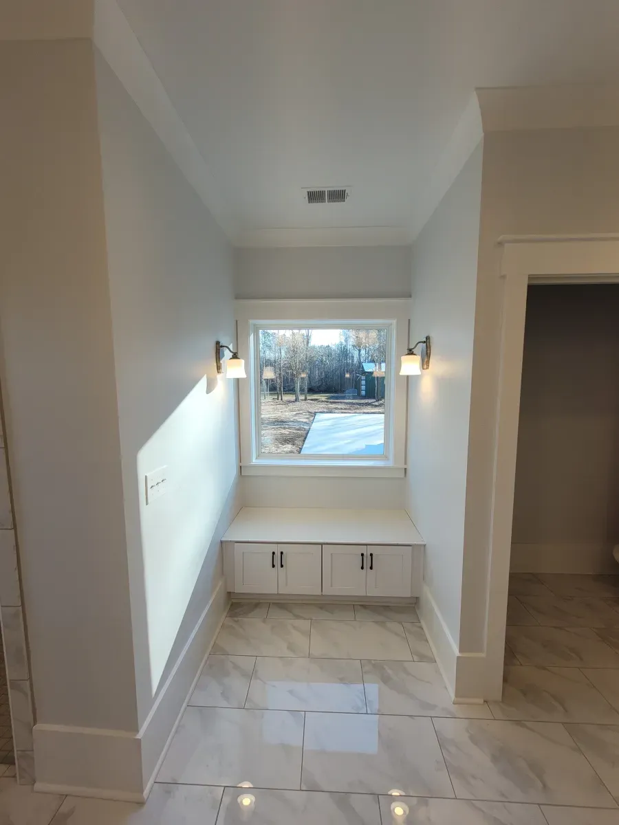 Hallway with window seat, white walls, marble floor. Two sconces flank the window, cabinetry below.
