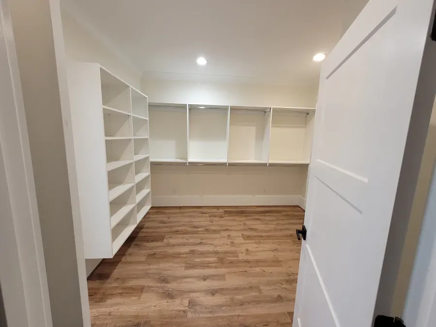 Empty white pantry with shelves, hardwood floors, and a partially open door.