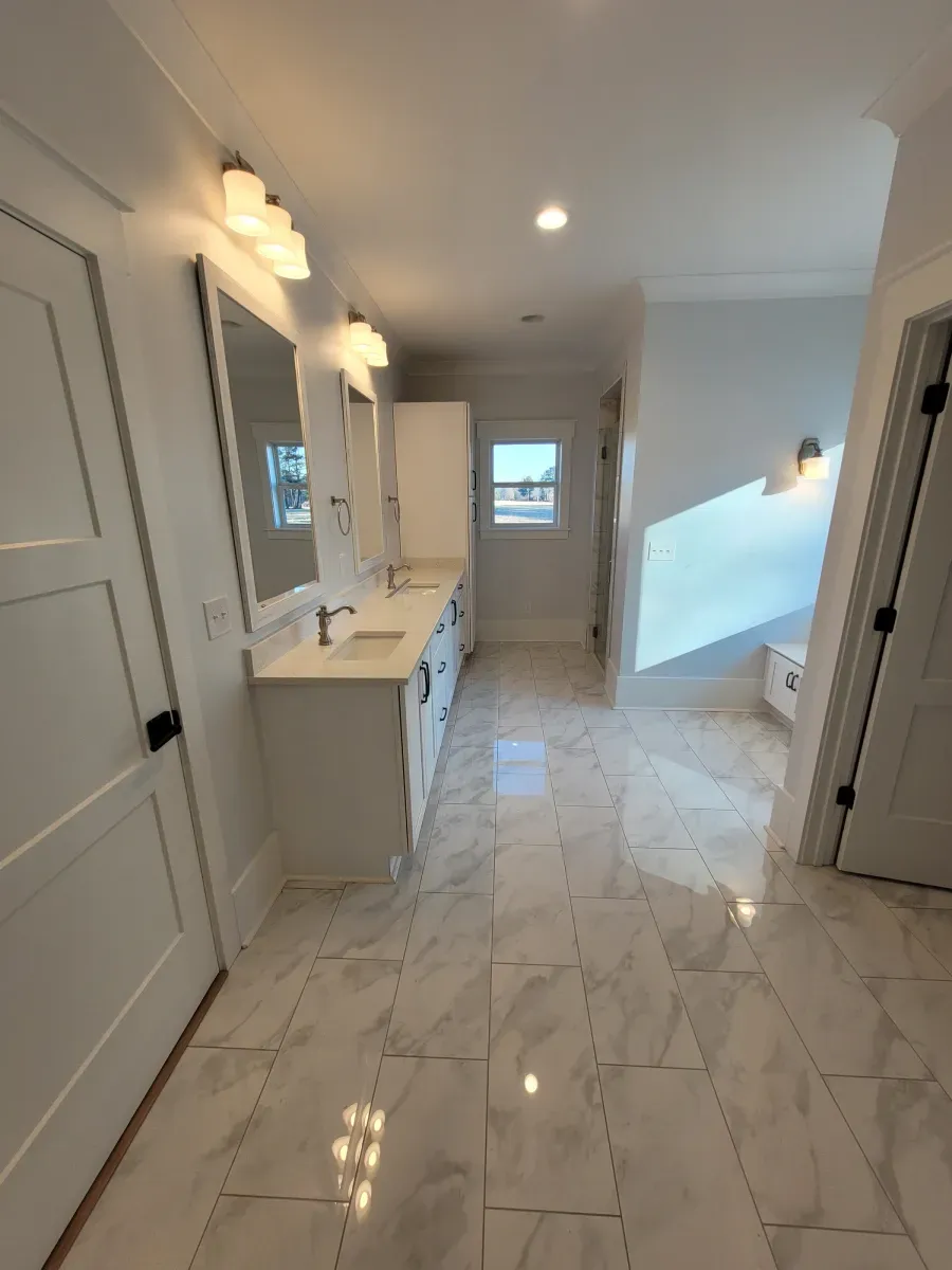 Bright white bathroom with marble floors, double sinks, and modern lighting.