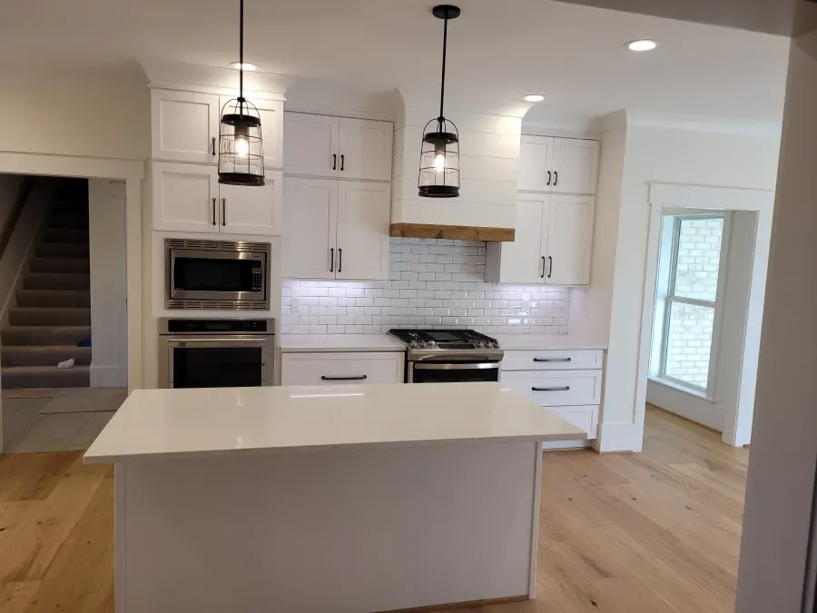White kitchen with island, cabinets, stainless steel appliances, wood floor, and two pendant lights.