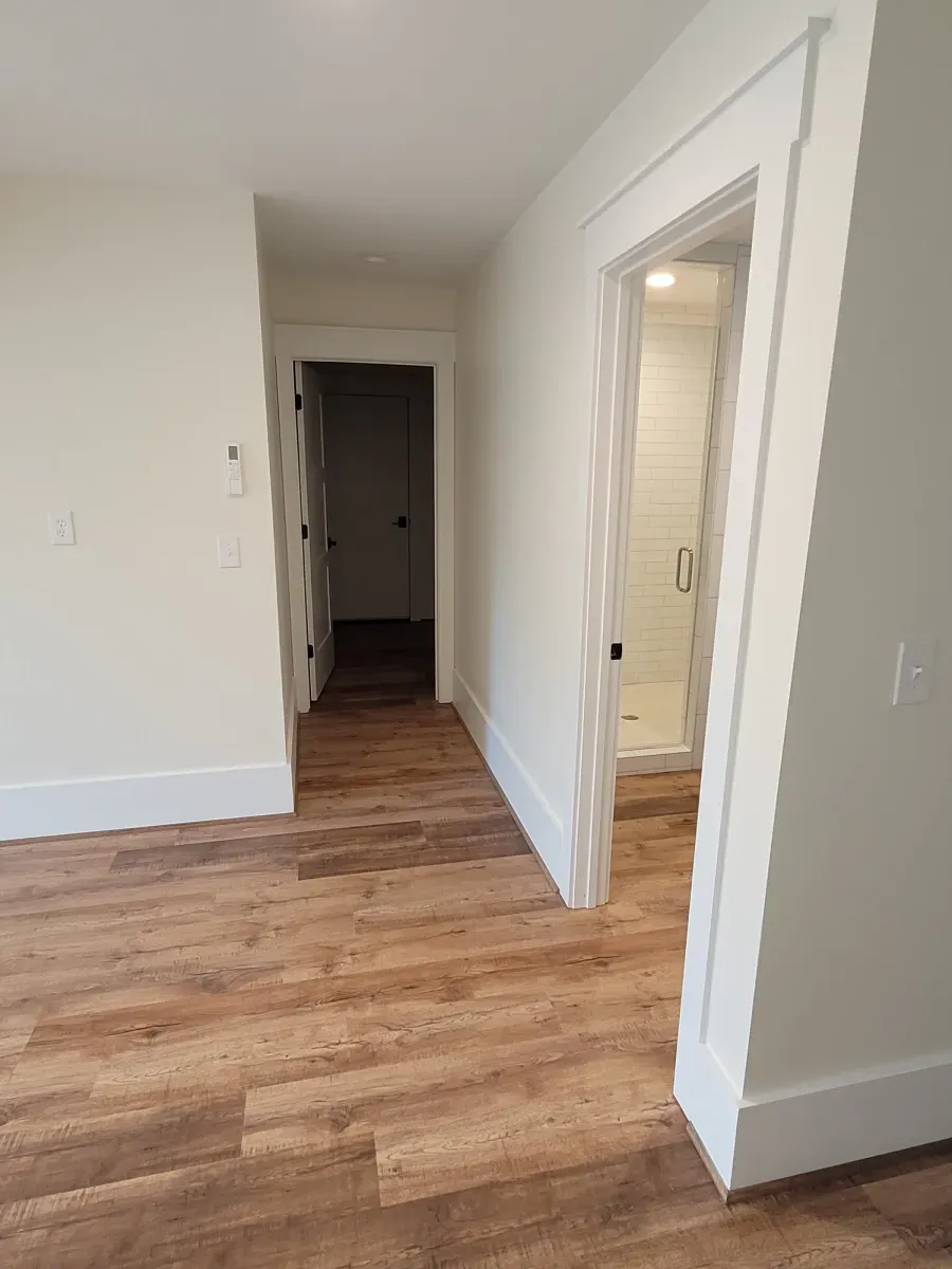 Hallway with wood floor, three white doors, and white walls.