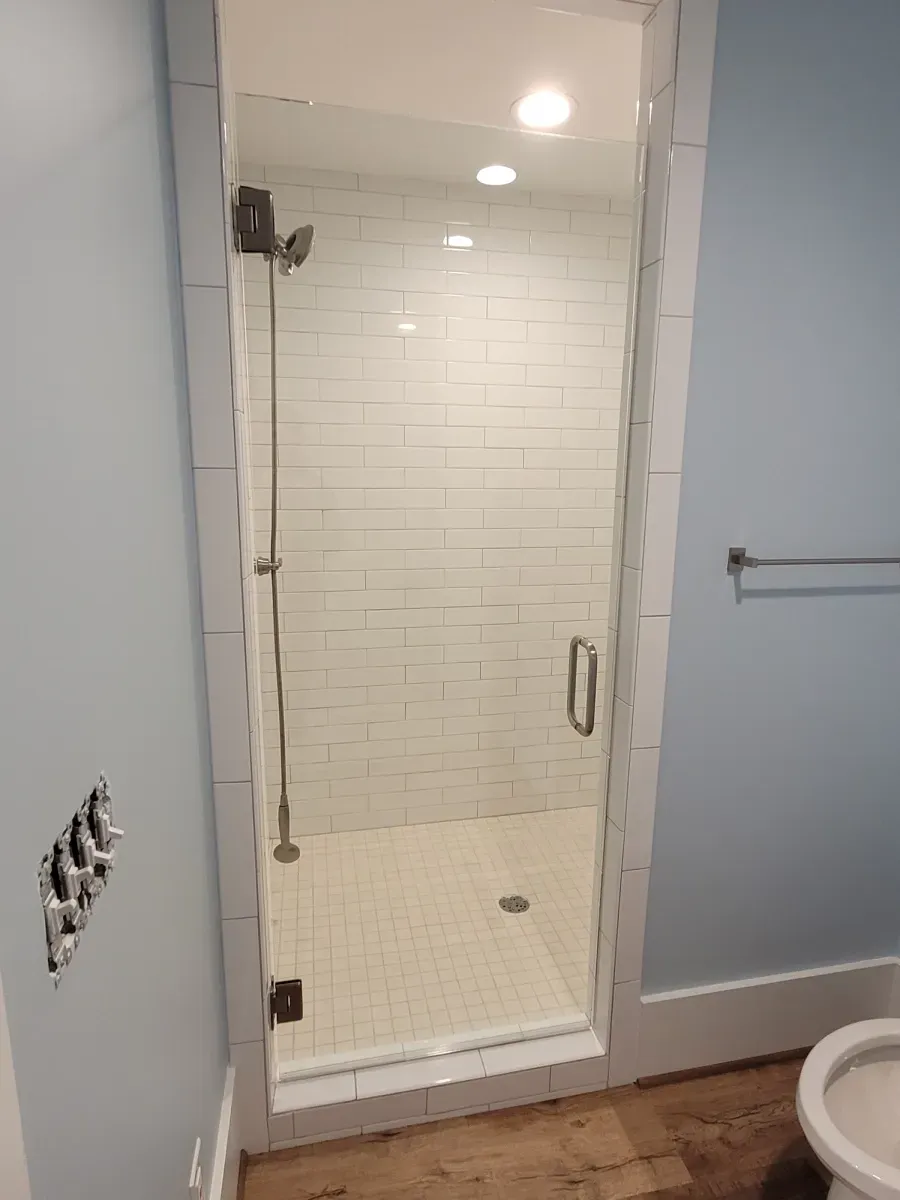 A glass shower enclosure with white subway tile walls in a bathroom with light blue walls and a towel rack.